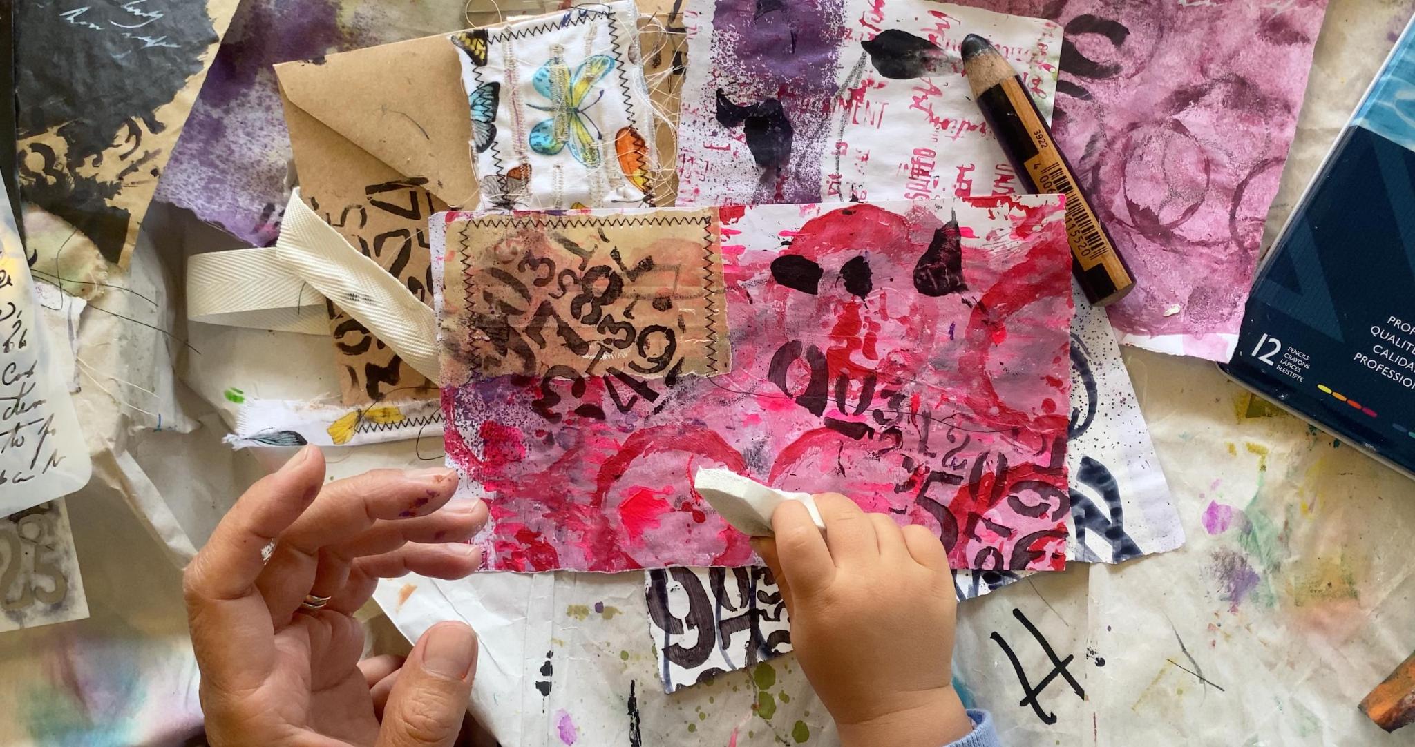 Tina's hands working on a mixed media junk journal page with red and pink paint, stamped numbers and collage elements