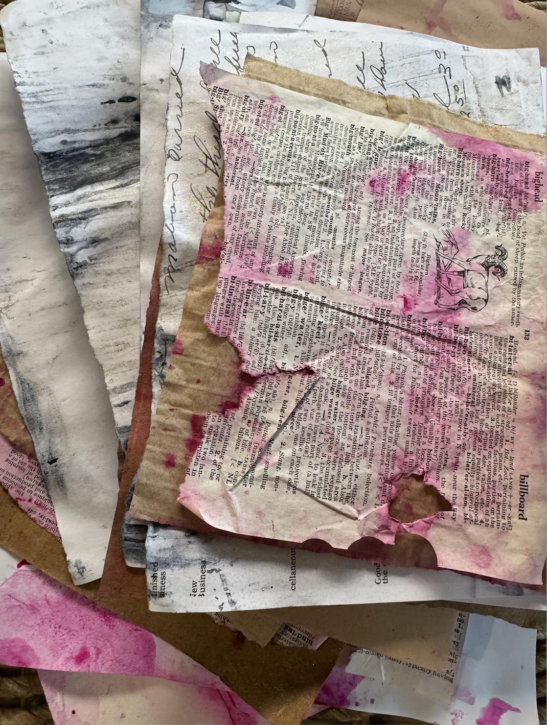 A stack of prepared junk journal papers — torn dictionary pages with pink paint washes and brown paper bags, layered and ready to use
