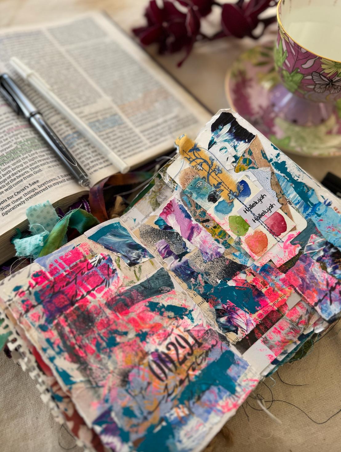 Open art journal beside a Bible with a floral teacup