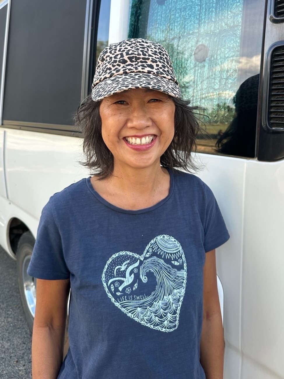 Tina smiling in front of the van she and her family travel in — creating Transforming Pages on the road